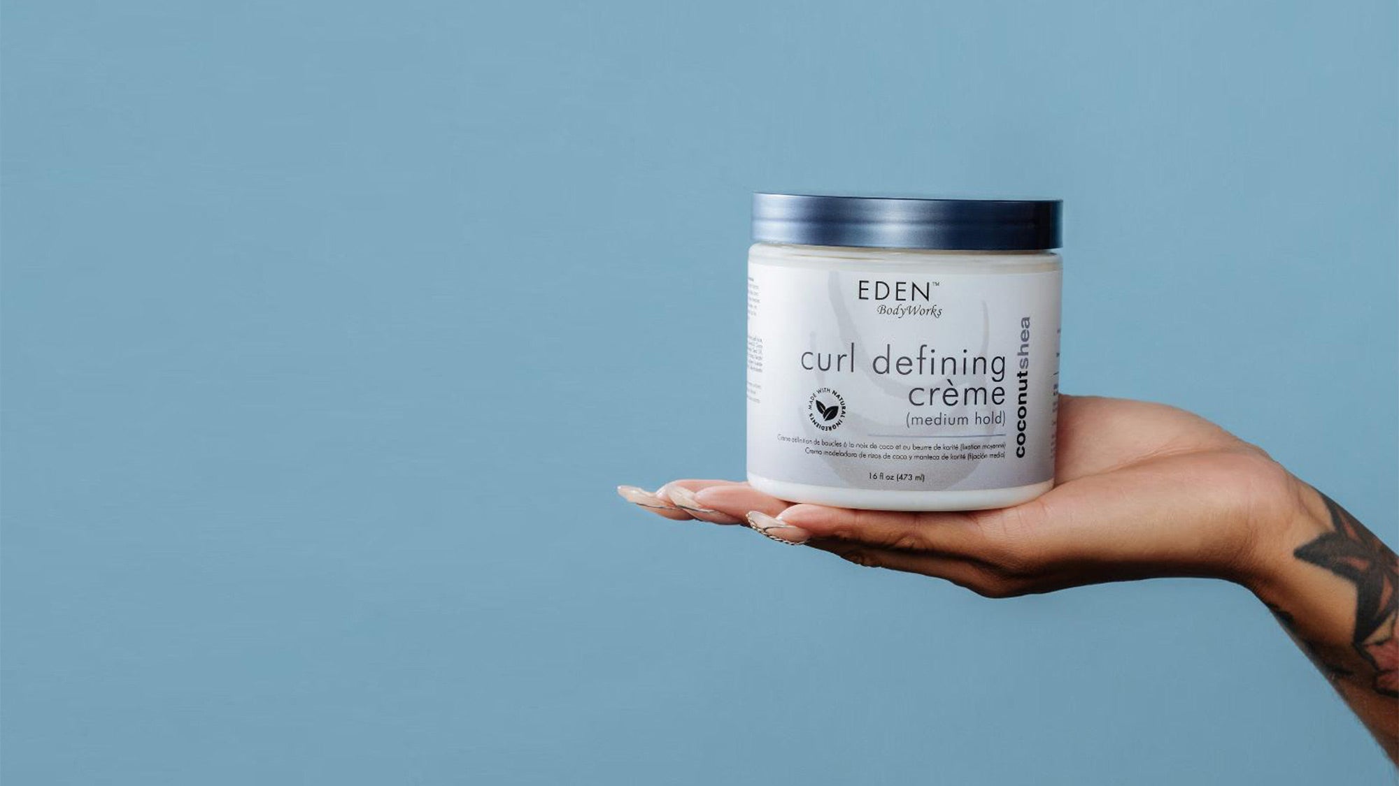 Hand holding a jar of Eden Bodyworks curl defining crème against a blue background